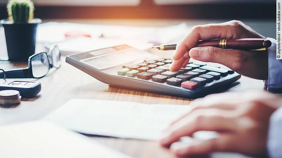 Ein Mann tippt etwas in einen Taschenrechner. Vor ihm liegt ein Blatt Papier.