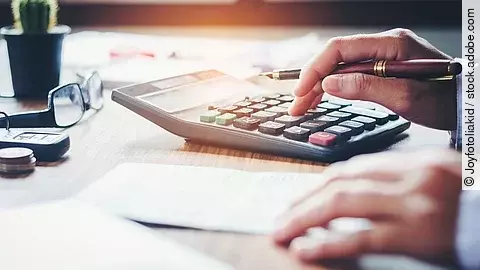 Ein Mann tippt etwas in einen Taschenrechner. Vor ihm liegt ein Blatt Papier.