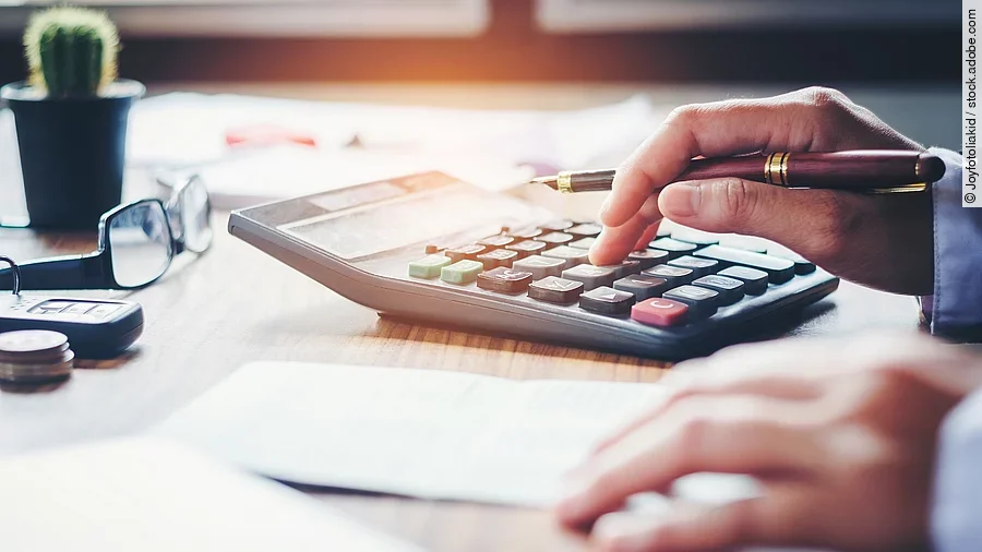 Ein Mann tippt etwas in einen Taschenrechner. Vor ihm liegt ein Blatt Papier.