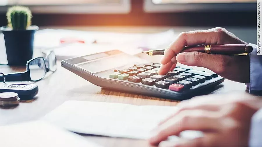 Ein Mann tippt etwas in einen Taschenrechner. Vor ihm liegt ein Blatt Papier.