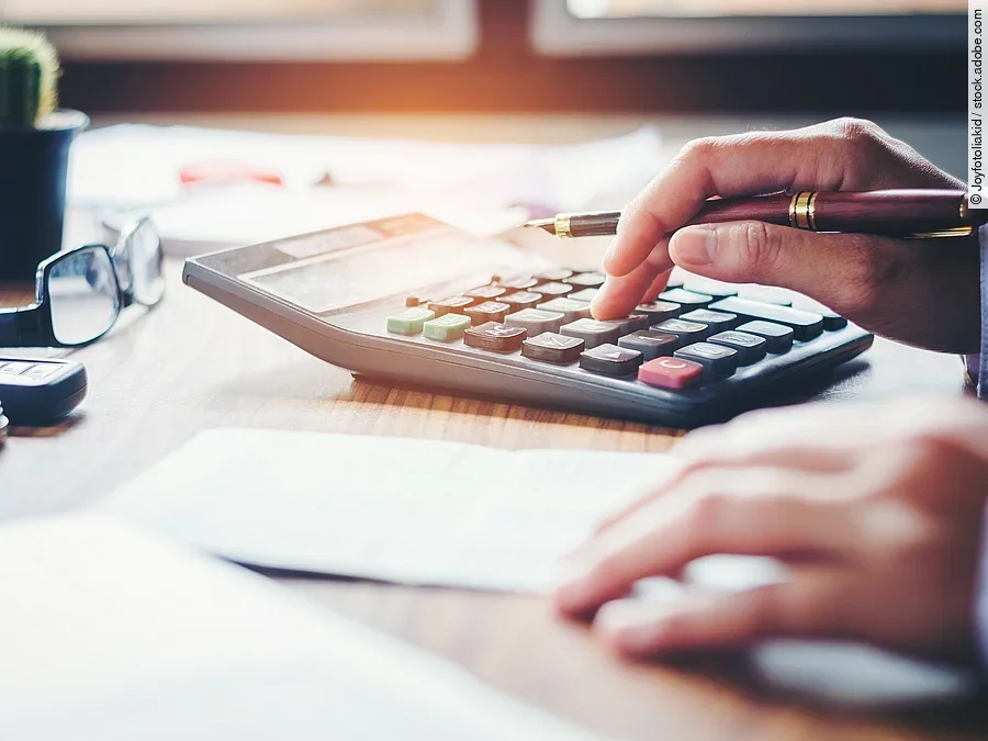 Ein Mann tippt etwas in einen Taschenrechner. Vor ihm liegt ein Blatt Papier.