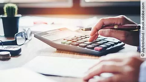 Ein Mann tippt etwas in einen Taschenrechner. Vor ihm liegt ein Blatt Papier.