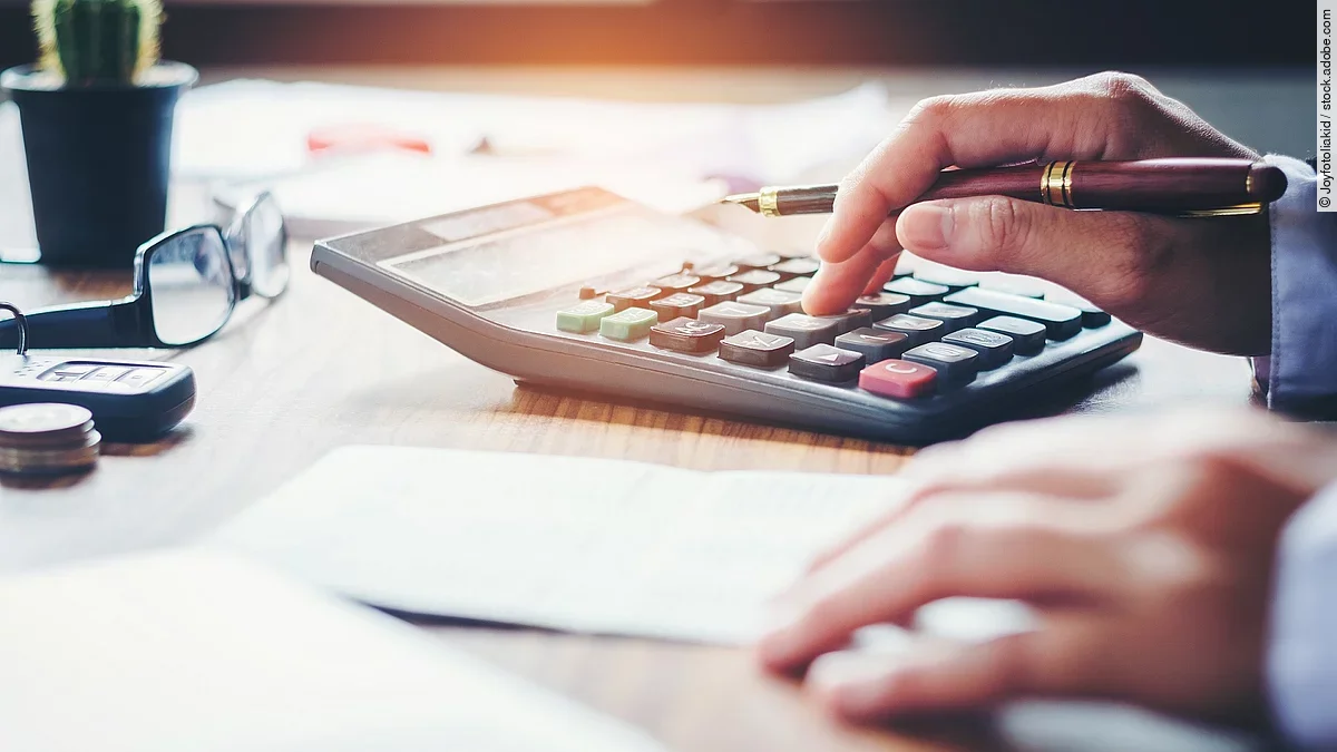 Rechnung Ein Mann tippt etwas in einen Taschenrechner. Vor ihm liegt ein Blatt Papier.