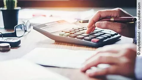 Rechnung Ein Mann tippt etwas in einen Taschenrechner. Vor ihm liegt ein Blatt Papier.