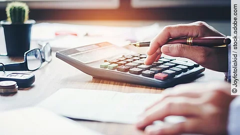 Ein Mann tippt etwas in einen Taschenrechner. Vor ihm liegt ein Blatt Papier.