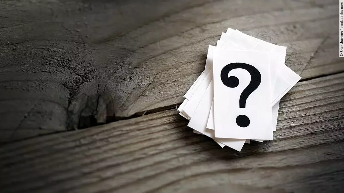 Weiße Karten mit Fragezeichen liegen auf einem Holztisch