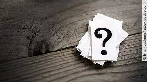 Weiße Karten mit Fragezeichen liegen auf einem Holztisch