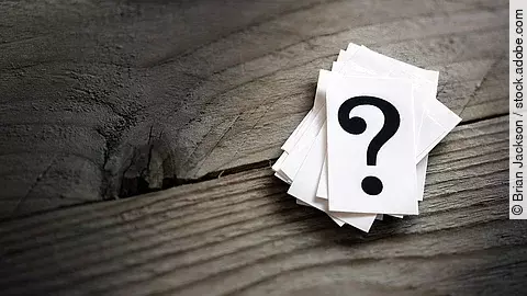 Weiße Karten mit Fragezeichen liegen auf einem Holztisch