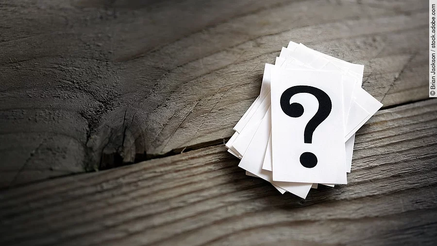 Weiße Karten mit Fragezeichen liegen auf einem Holztisch