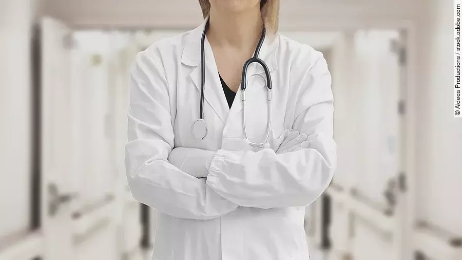 Ärztin in Arbeitskleidung steht mit verschränkten Armen im Krankenhausgang.