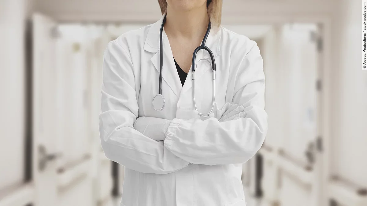 Ärztin in Arbeitskleidung steht mit verschränkten Armen im Krankenhausgang.