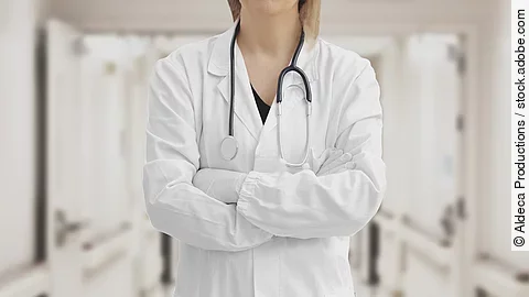 Ärztin in Arbeitskleidung steht mit verschränkten Armen im Krankenhausgang.