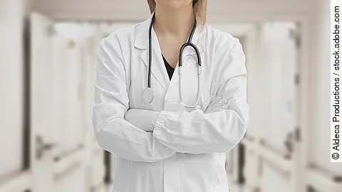 Ärztin Ärztin in Arbeitskleidung steht mit verschränkten Armen im Krankenhausgang.