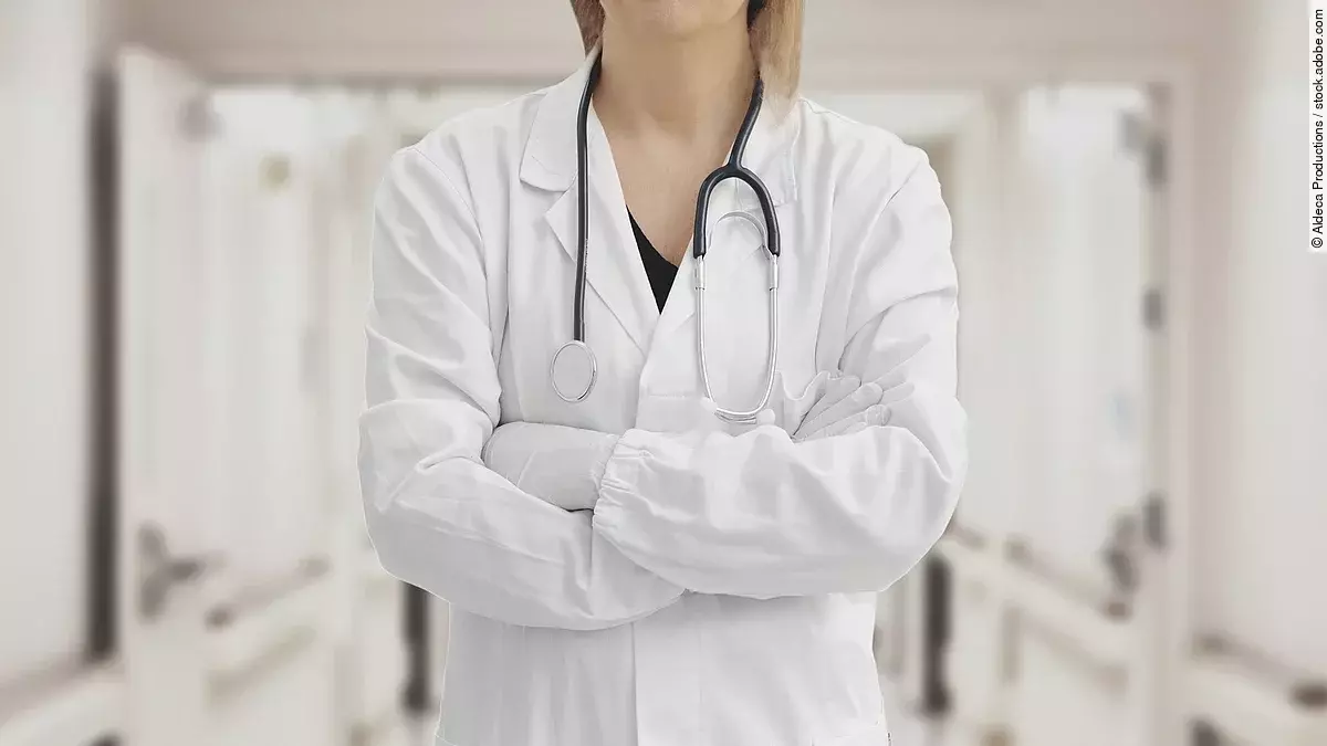 Ärztin in Arbeitskleidung steht mit verschränkten Armen im Krankenhausgang.