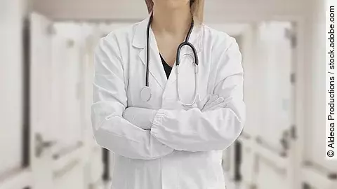 Ärztin in Arbeitskleidung steht mit verschränkten Armen im Krankenhausgang.