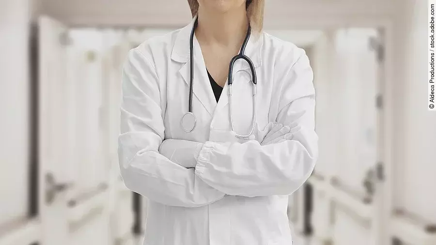 Ärztin in Arbeitskleidung steht mit verschränkten Armen im Krankenhausgang.