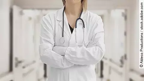 Ärztin in Arbeitskleidung steht mit verschränkten Armen im Krankenhausgang.