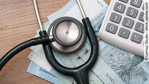 Taschenrechner und Stethoskop liegen auf Geldscheinen