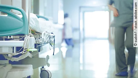 Krankenhausflur mit einem leeren Bett und einer Pflegefachkraft