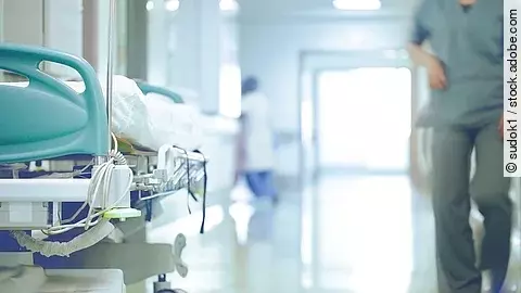 Krankenhausflur mit einem leeren Bett und einer Pflegefachkraft