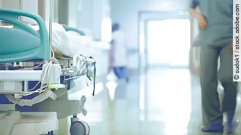 Krankenhausflur mit einem leeren Bett und einer Pflegefachkraft