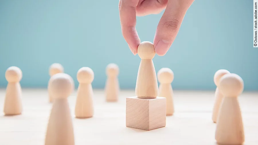 Leader Mehrere Holzfiguren, die Personen darstellen. Eine der Figuren steht auf einem kleinen Würfel.