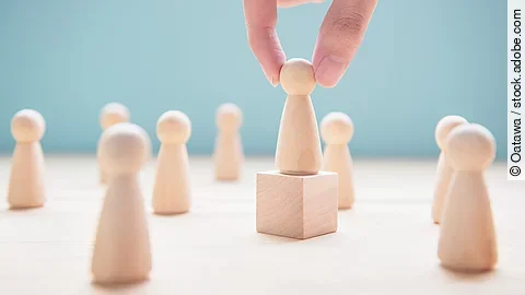 Leader Mehrere Holzfiguren, die Personen darstellen. Eine der Figuren steht auf einem kleinen Würfel.