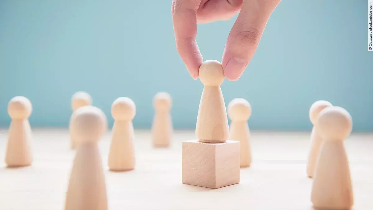 Mehrere Holzfiguren, die Personen darstellen. Eine der Figuren steht auf einem kleinen Würfel.