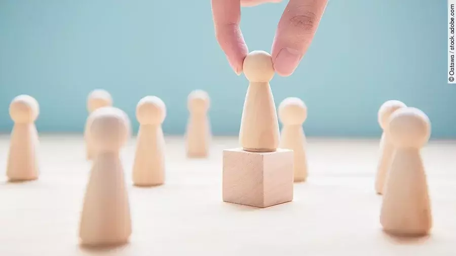 Leader Mehrere Holzfiguren, die Personen darstellen. Eine der Figuren steht auf einem kleinen Würfel.