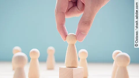 Leader Mehrere Holzfiguren, die Personen darstellen. Eine der Figuren steht auf einem kleinen Würfel.