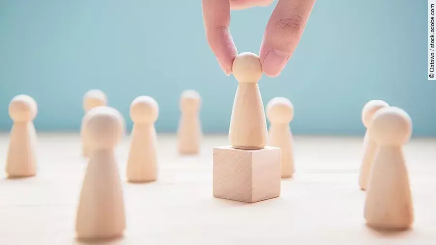 Leader Mehrere Holzfiguren, die Personen darstellen. Eine der Figuren steht auf einem kleinen Würfel.