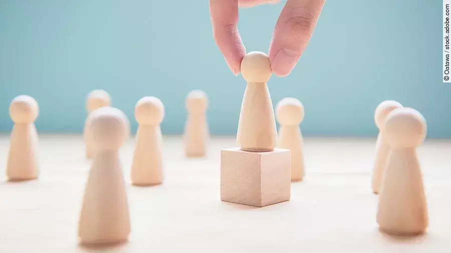 Leader Mehrere Holzfiguren, die Personen darstellen. Eine der Figuren steht auf einem kleinen Würfel.