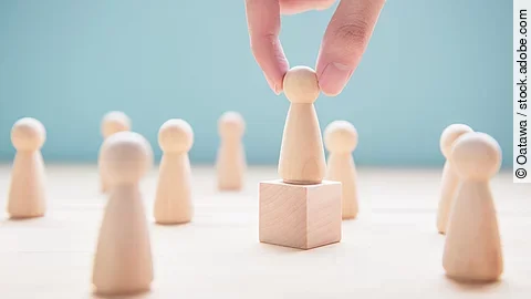 Leader Mehrere Holzfiguren, die Personen darstellen. Eine der Figuren steht auf einem kleinen Würfel.