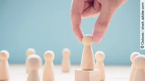 Mehrere Holzfiguren, die Personen darstellen. Eine der Figuren steht auf einem kleinen Würfel.