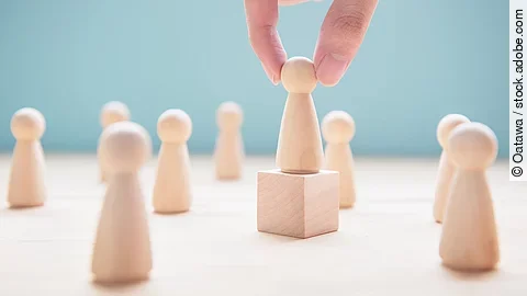 Mehrere Holzfiguren, die Personen darstellen. Eine der Figuren steht auf einem kleinen Würfel.