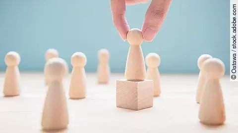 Mehrere Holzfiguren, die Personen darstellen. Eine der Figuren steht auf einem kleinen Würfel.