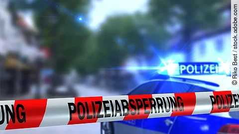 Polizeiabsperrung Ein rot-weißes Band mit der Beschriftung "Polizeiabsperrung". Im Hintergrund ist ein Polizeiauto zu sehen.