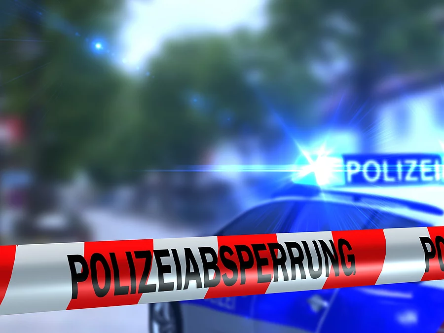 Polizeiabsperrung Ein rot-weißes Band mit der Beschriftung "Polizeiabsperrung". Im Hintergrund ist ein Polizeiauto zu sehen.