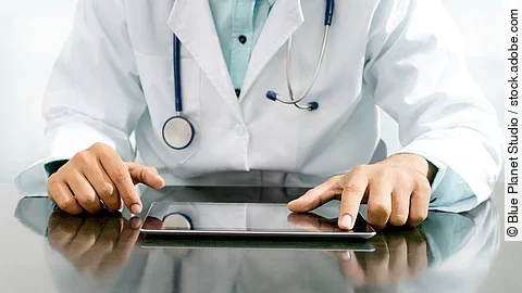 Arzt sitzt an einem Tisch und vor ihm liegt ein Tablet,