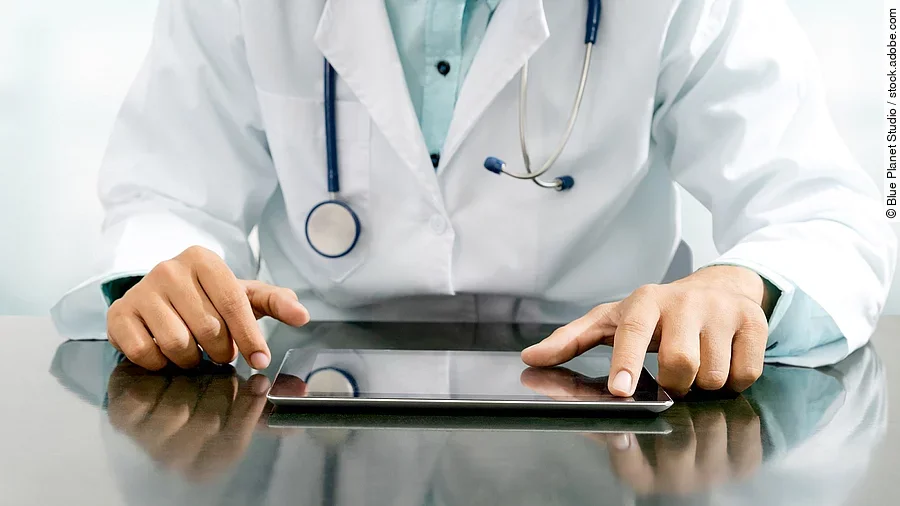 Arzt sitzt an einem Tisch und vor ihm liegt ein Tablet,