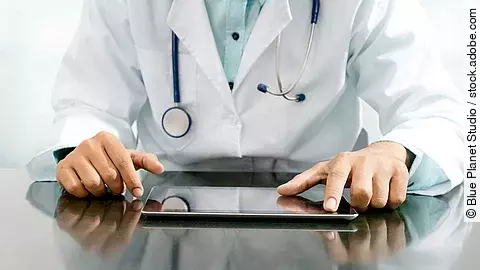 Arzt sitzt an einem Tisch und vor ihm liegt ein Tablet,
