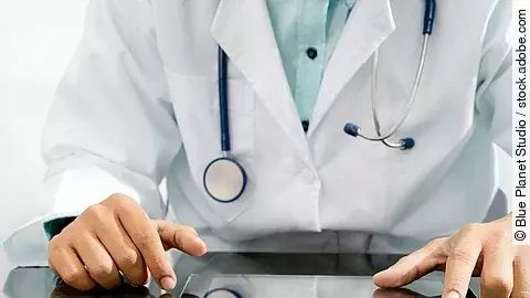 Arzt sitzt an einem Tisch und vor ihm liegt ein Tablet,