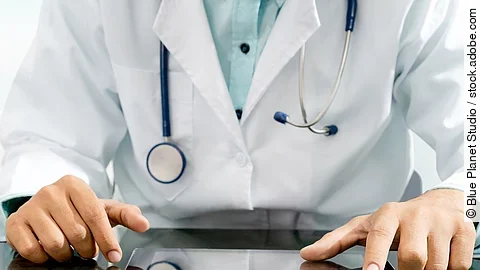 Arzt sitzt an einem Tisch und vor ihm liegt ein Tablet,