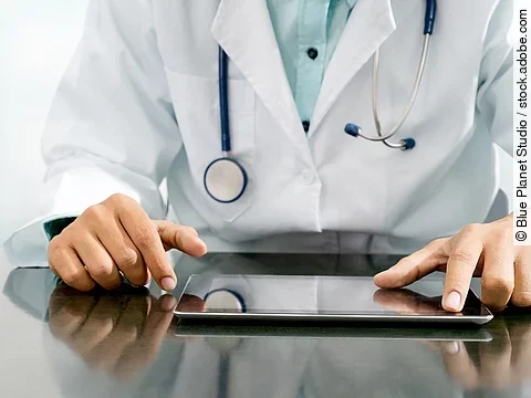 Arzt sitzt an einem Tisch und vor ihm liegt ein Tablet,