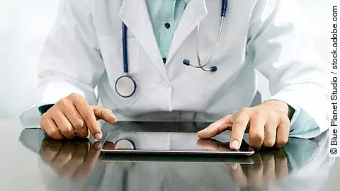 Arzt sitzt an einem Tisch und vor ihm liegt ein Tablet,