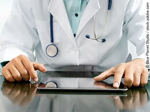 Arzt sitzt an einem Tisch und vor ihm liegt ein Tablet,