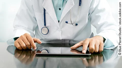 Arzt sitzt an einem Tisch und vor ihm liegt ein Tablet,