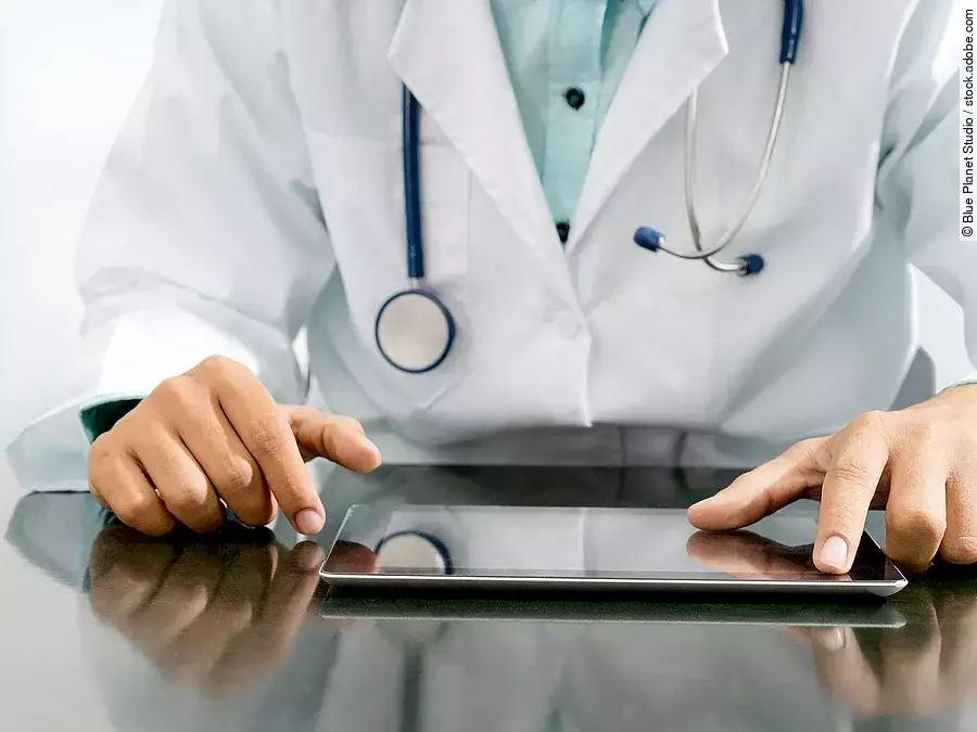 Arzt sitzt an einem Tisch und vor ihm liegt ein Tablet,