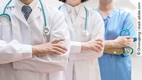 Drei Personen stehen nebeneinander. Links ein Arzt in weißem Kittel, in der Mitte eine Ärztin mit weißem Kittel, rechts eine Krankenschwester in blauem Kasack. Es sind jeweils nur die Torsi zu sehen. Alle drei haben ein Stethoskop.