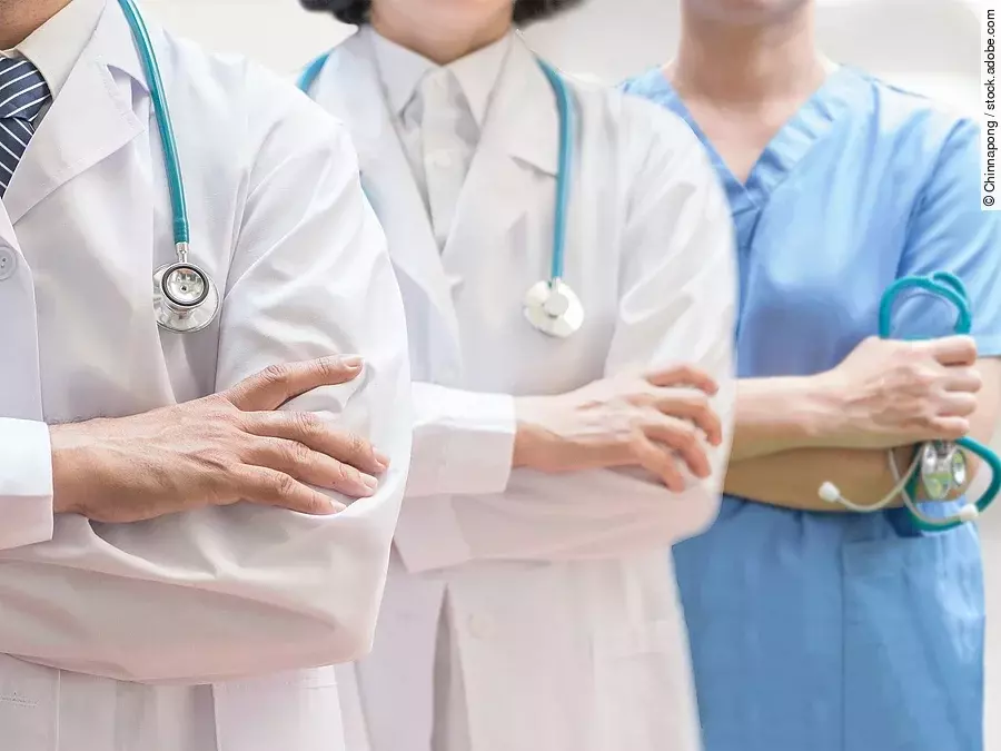 Klinikpersonal Drei Personen stehen nebeneinander. Links ein Arzt in weißem Kittel, in der Mitte eine Ärztin mit weißem Kittel, rechts eine Krankenschwester in blauem Kasack. Es sind jeweils nur die Torsi zu sehen. Alle drei haben ein Stethoskop.